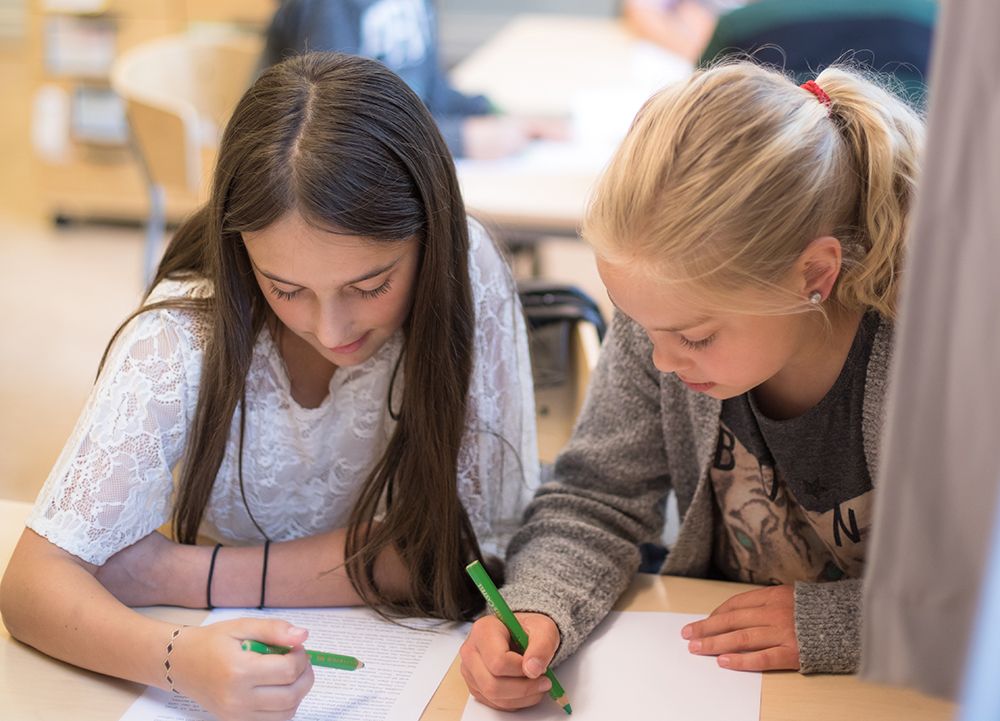 Två barn sitter och skriver på varsitt papper